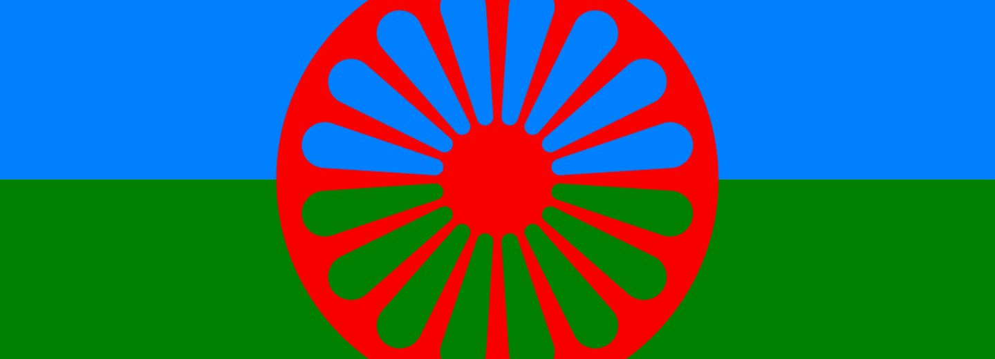 Romska flaggan, bakgrundens övre del är blå och den undre delen är grön. Framför finns röd ihålig cirkelformad symbol.