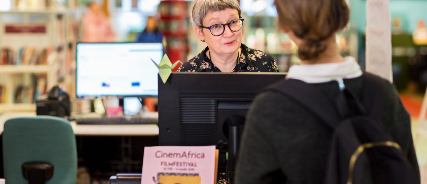 Kvinna som lånar en bok på ett bibliotek.