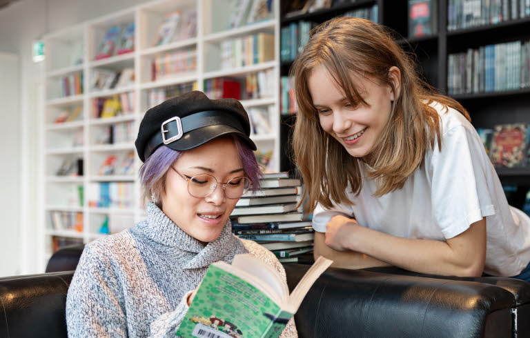 TvÃ¥ ungdomar pÃ¥ ett bibliotek tittar i en bok tillsammans