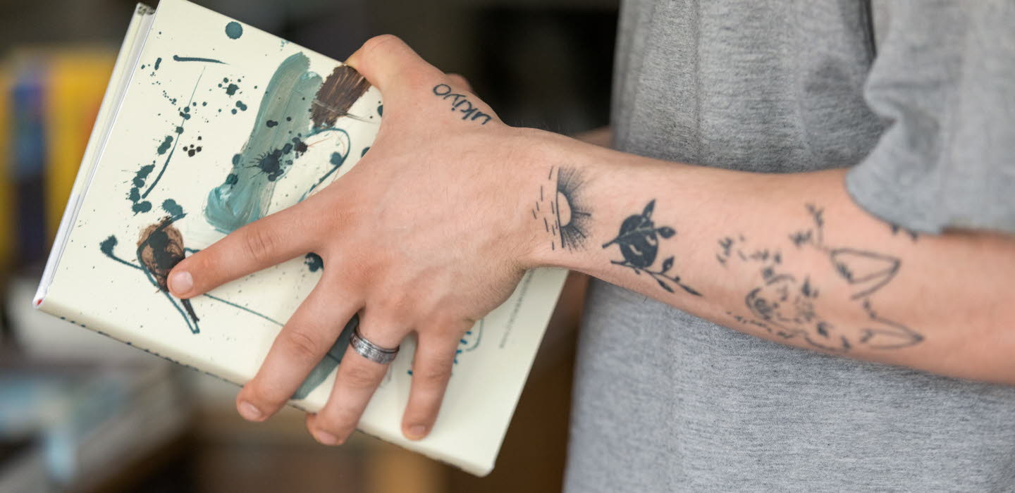 Tatuerade armar som håller i en bok.