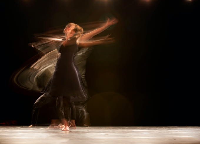 Dansande kvinna fotad med lång slutartid, mörk bakgrund.