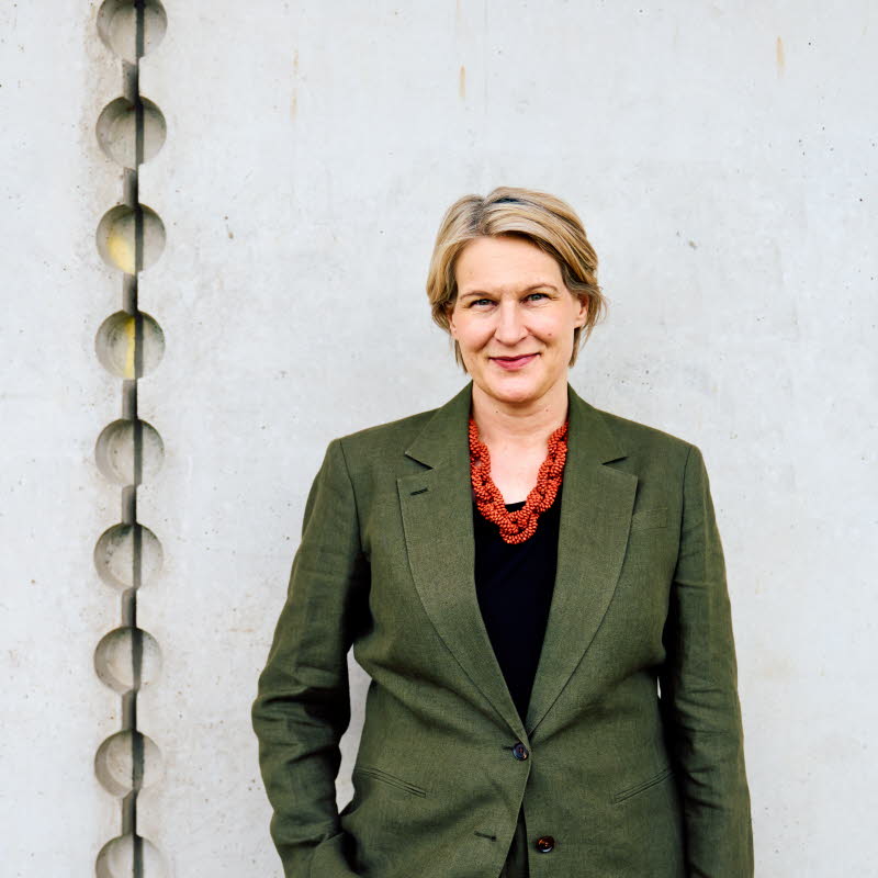 Pressbild på Kajsa Ravin som står framför en grå vägg.