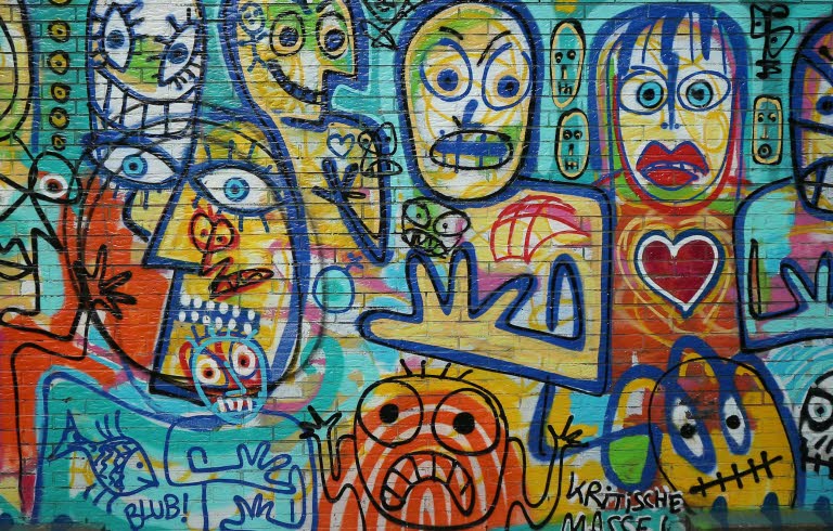 Tegelvägg fylld med grafitti med målade ansikten i glada färger.