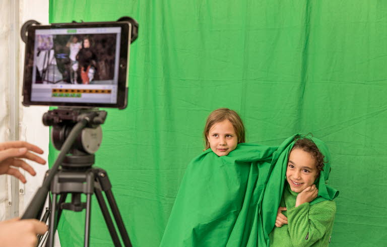 Två barn med gröna kläder blir filmade mot en grön vägg.