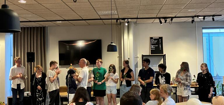 Ungdomar med blommor i händerna står uppradade framför en publik.