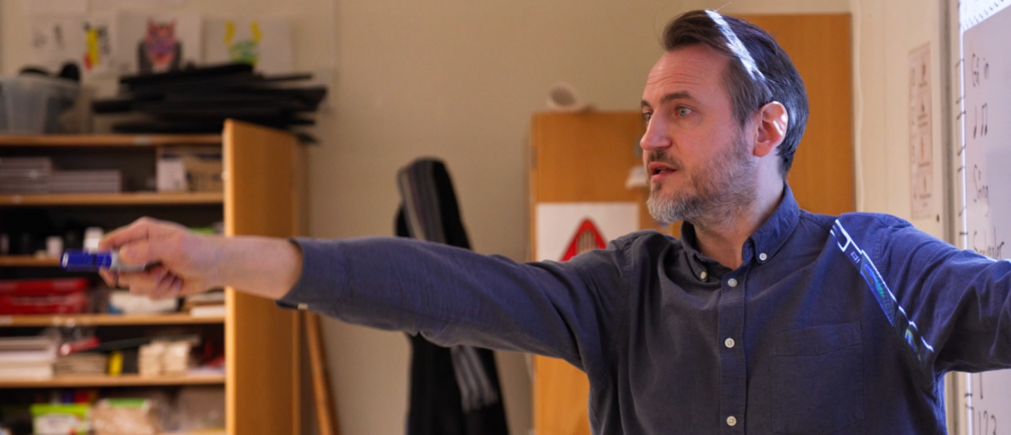 Manlig lärare pekar med en penna i ett klassrum.