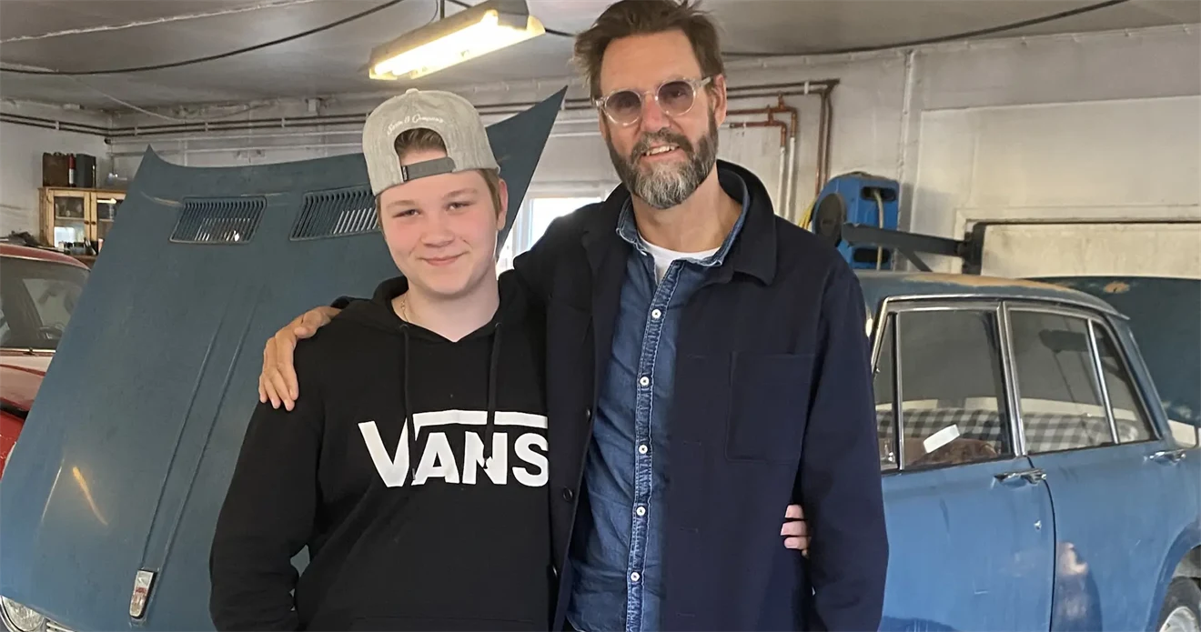 En ung kille står tillsammans med en författare framför en bil med öppen motorhuv.