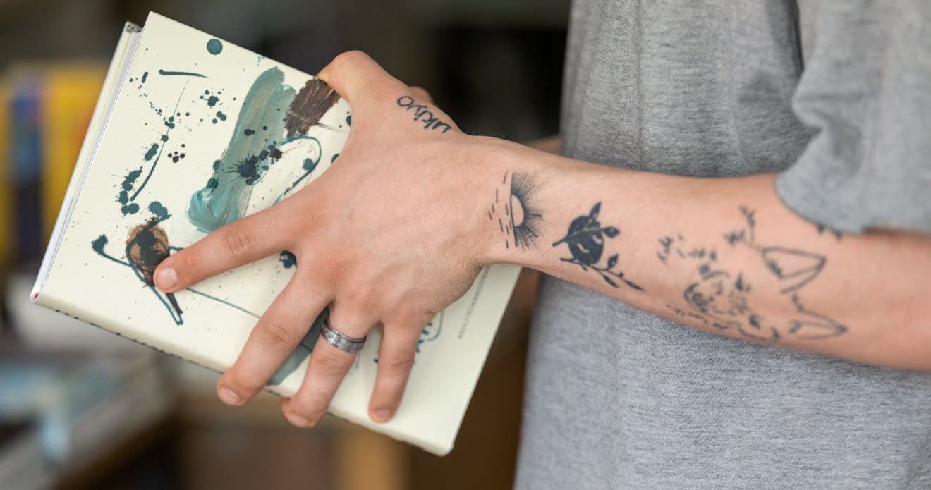 Tatuerade armar som håller i en bok.