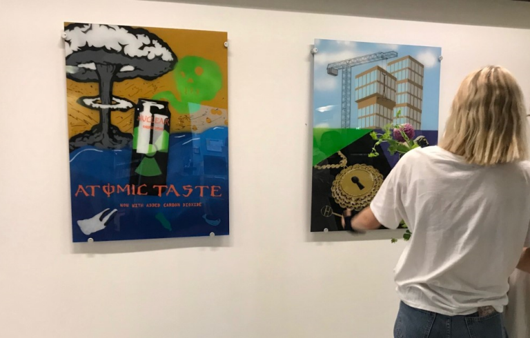 Två personer ser på tavlor som hänger på en vägg.