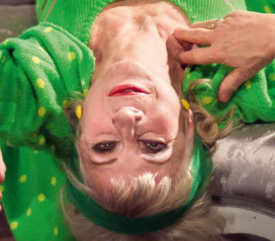 Book cover of "Vem tror hon att hon är": it's a photo of a women lies upside down on a couch wearing a green sweatsuit with green dots, smoking a cigarette.