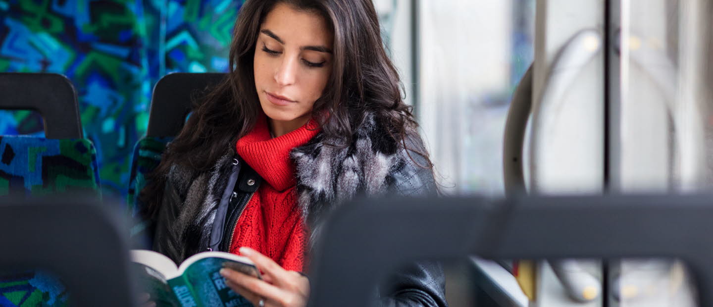 Kvinna på buss läser en bok.