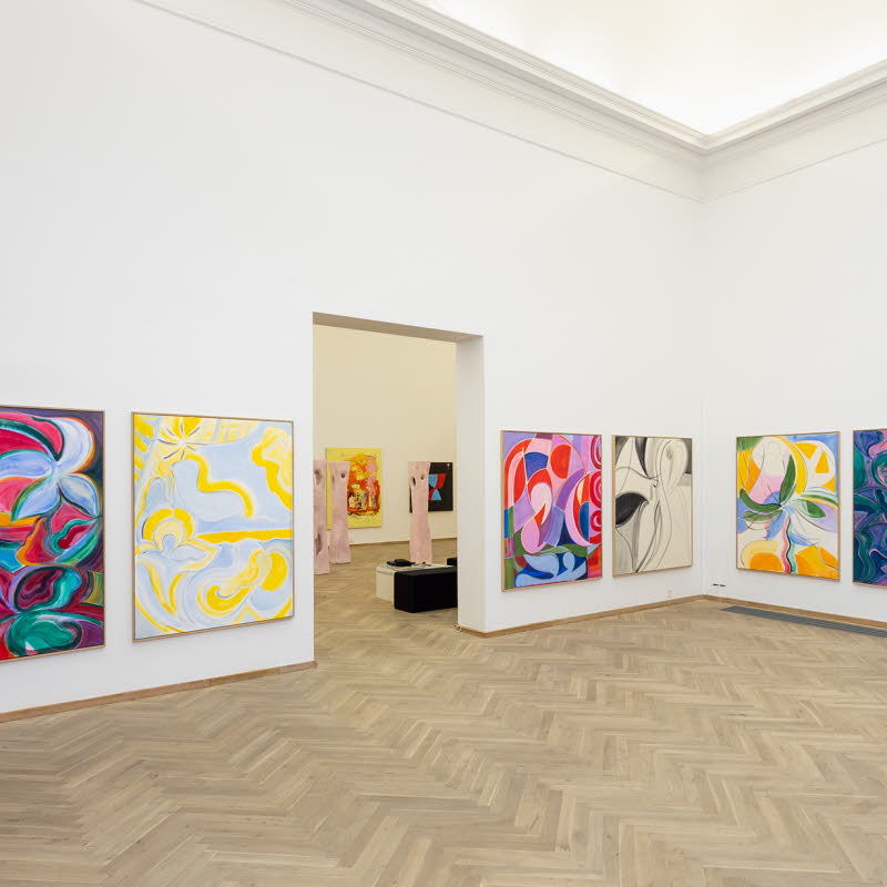 Bild på en utställning med sju stora färgglada målningar.