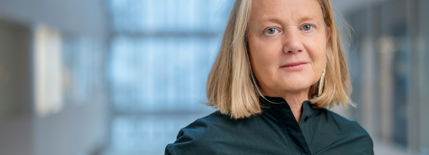 Medelålderskvinna i halvfigur. Blond page och mörkblå blus.