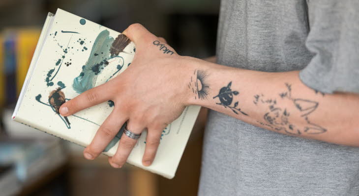 Tatuerade armar som håller i en bok.