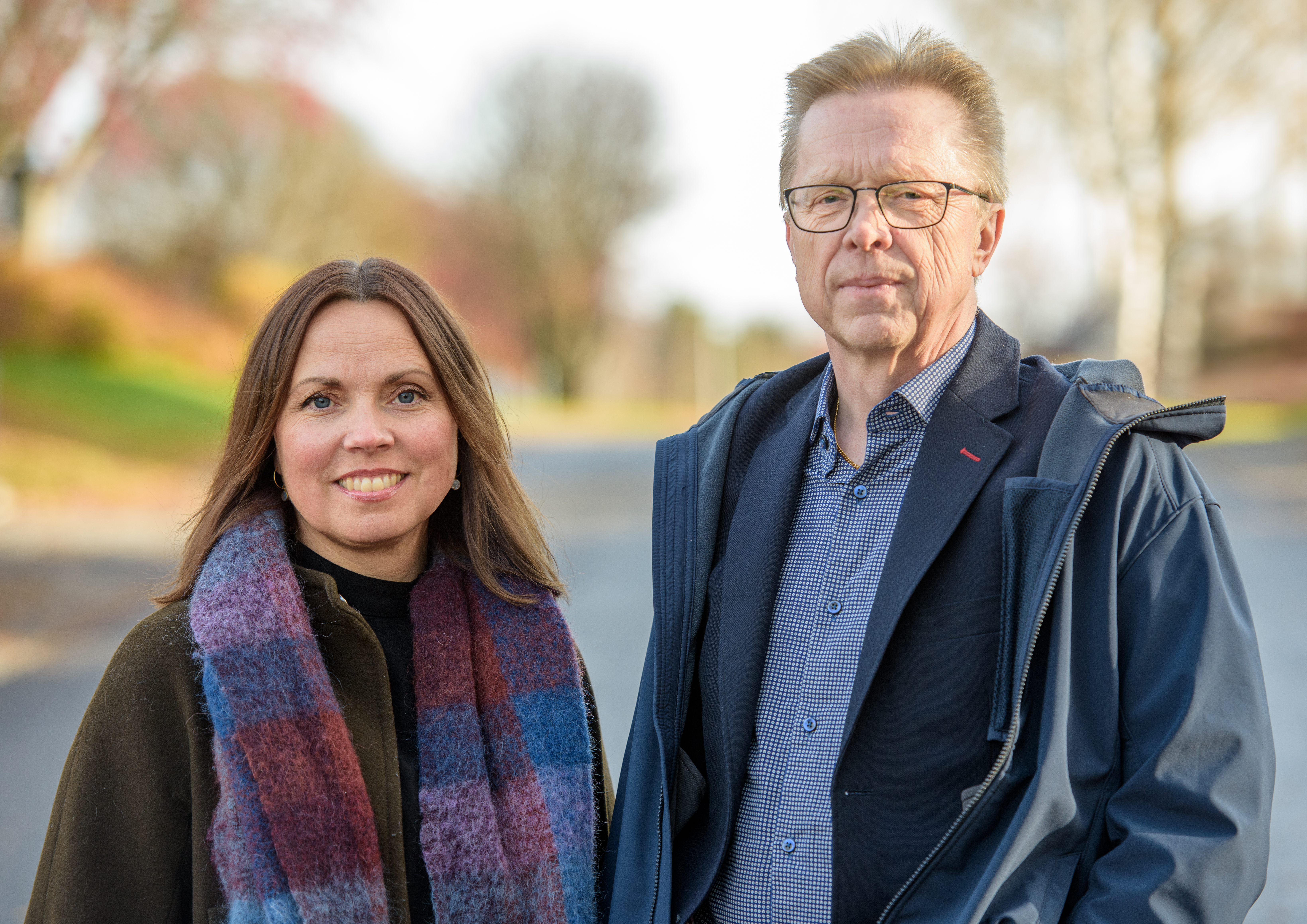 Portr&auml;ttbild p&aring; kvinna med l&aring;ngt h&aring;r och man med kort h&aring;r och glas&ouml;gon, utomhus.