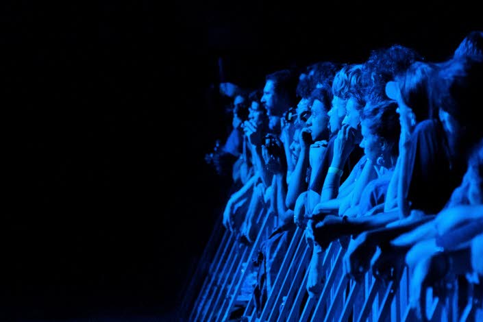 Bild på en publikrad i blått ljus och som lutar sig mot staketet innan scen. 