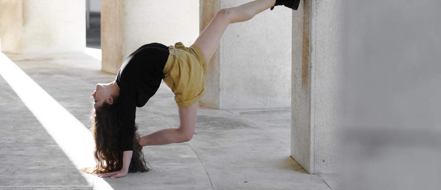 Akrobatisk dansrörelse av Marina Cherry med foten mot en betongpelare.