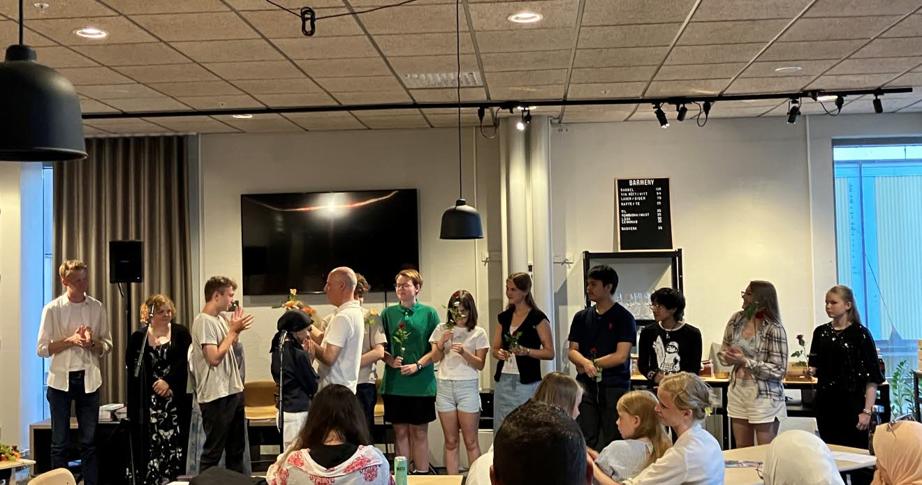 Ungdomar med blommor i händerna står uppradade framför en publik.