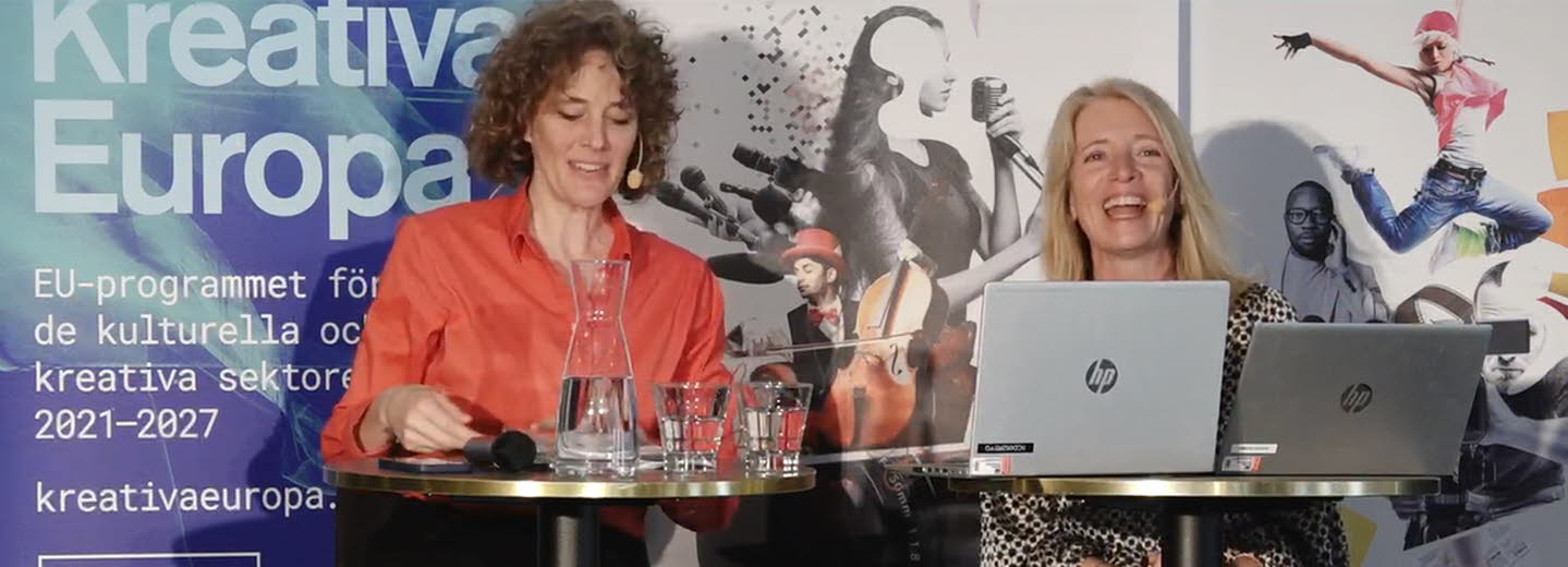I bild Bongi MacDermott och Anette Novak. Bongi och Anette sitter på scen och samtalar.
