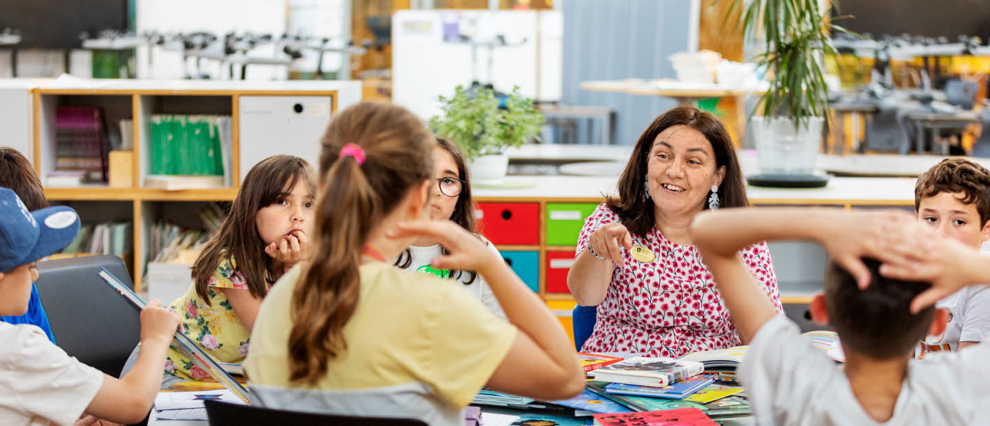 Lärade och elever samtalar kring ett bord fullt av böcker.