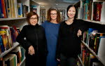 Tre kvinnor står mellan bokhyllor, tittar in i kameran