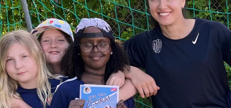 Barn i fotbollskläder som poserar tillsammans med en kvinna i ett fotbollsmål.