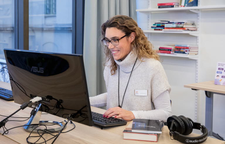 Kvinnlig bibliotekarie sitter framför datorn och tar del samtal som pågår på skärmen.