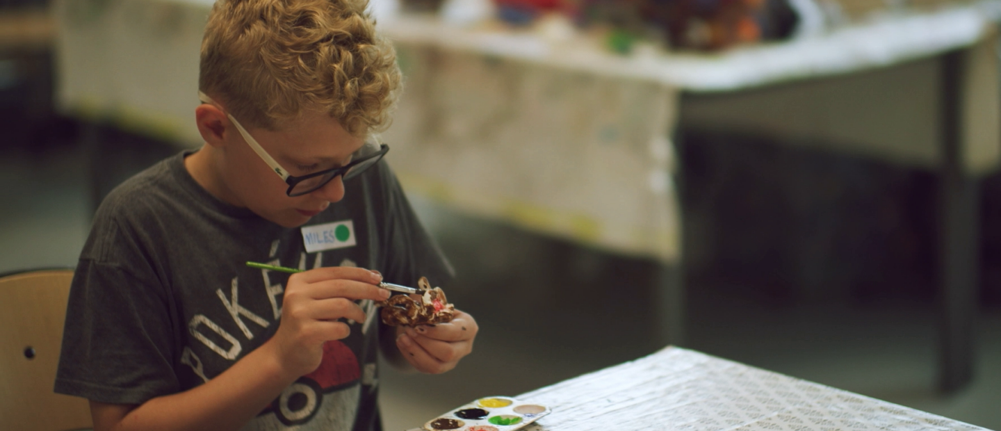 Pojke sitter vid ett bord och målar på figurer.