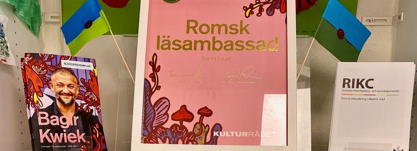 Hylla från bibliotek med intyg på att biblioteket är romsk läsambassad.