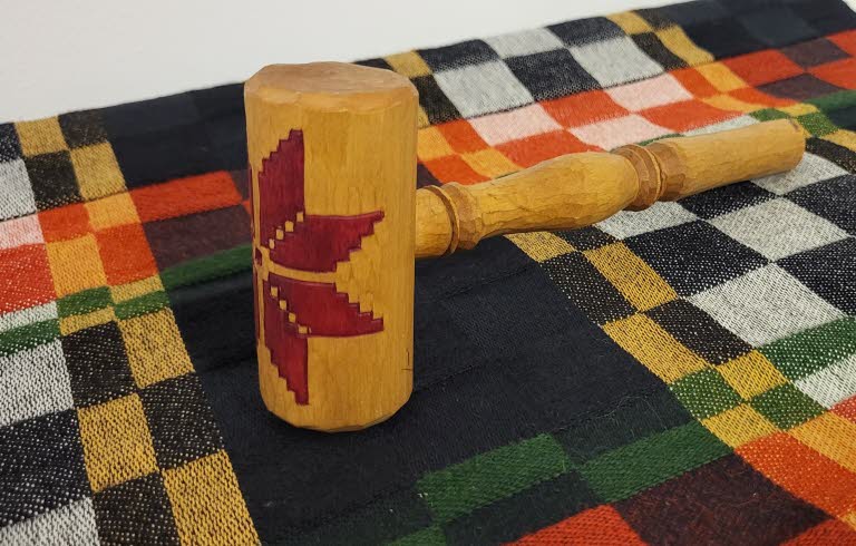 Träklubba dekorerad med röd stjärna, liggande på en färgglad rutmönstrad textil.