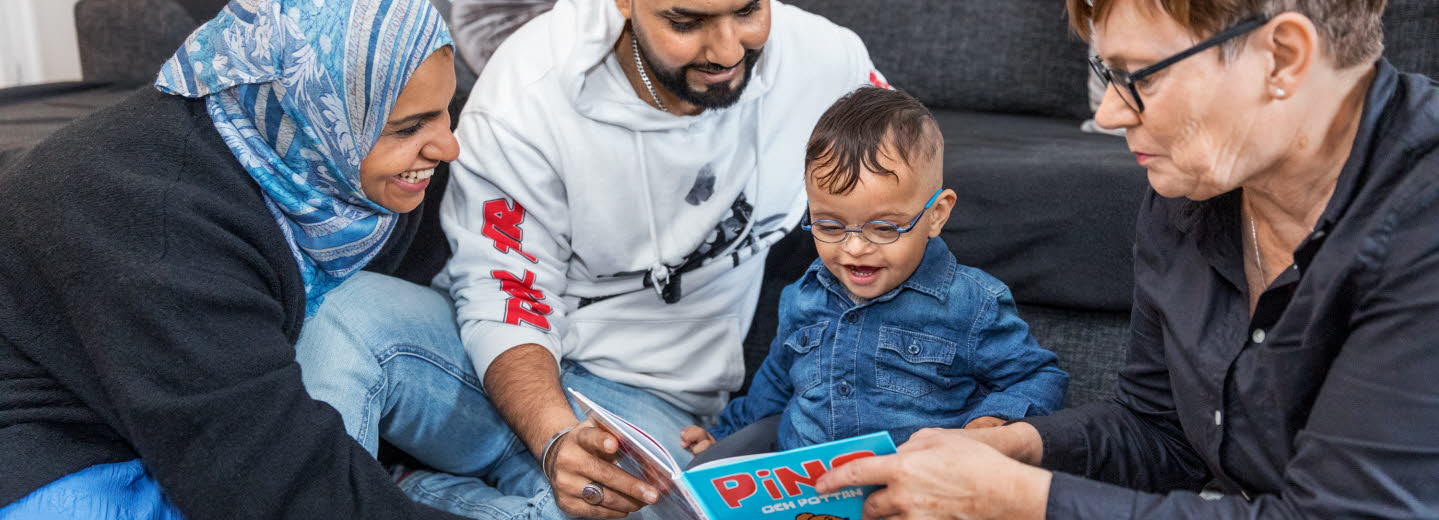 Två föräldrar läser tillsammans med bibliotekarie för ett yngre barn. 