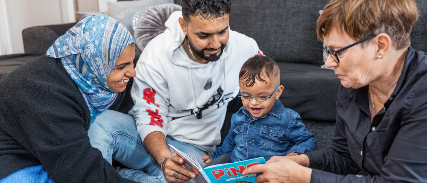 Två föräldrar läser tillsammans med bibliotekarie för ett yngre barn. 