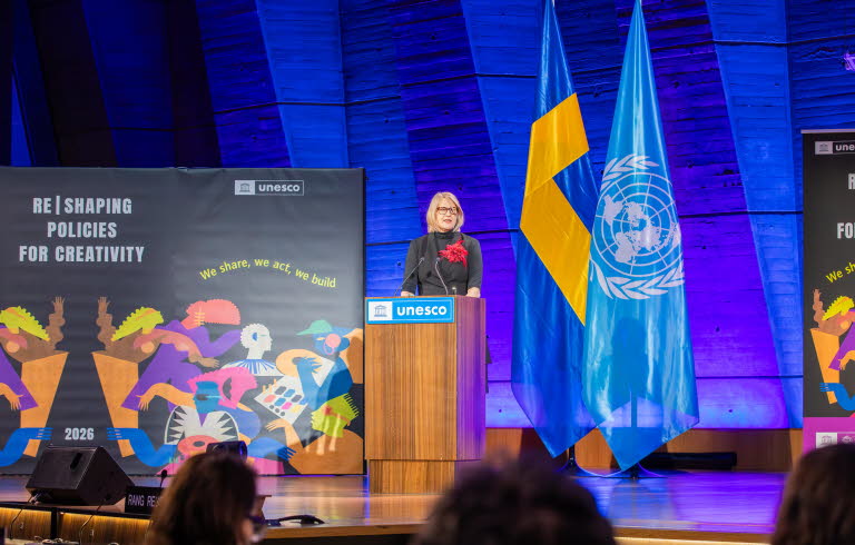 Kvinna som talar för en sittande publik. Unescos textlogotyp på talarstolen.