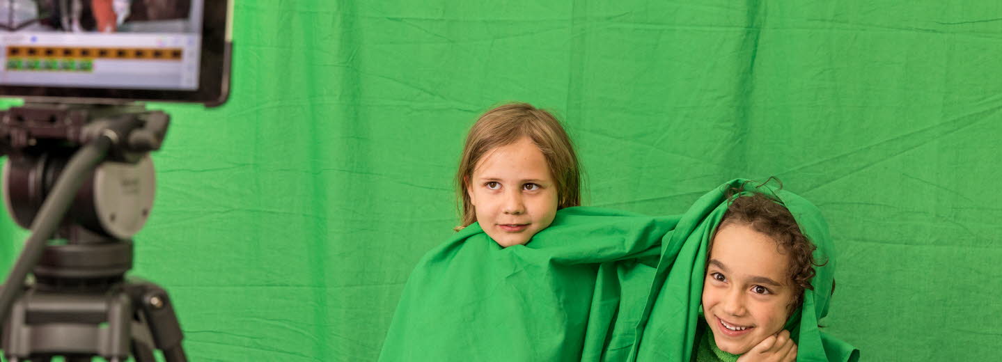 Två barn med gröna kläder blir filmade mot en grön vägg.