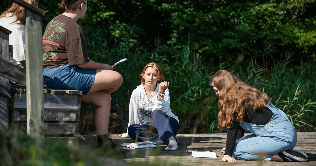 Ungdomar med böcker som sitter och pratar på ett trädäck.
