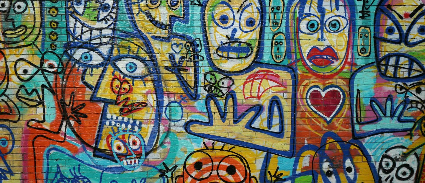 Tegelvägg fylld med grafitti med målade ansikten i glada färger.