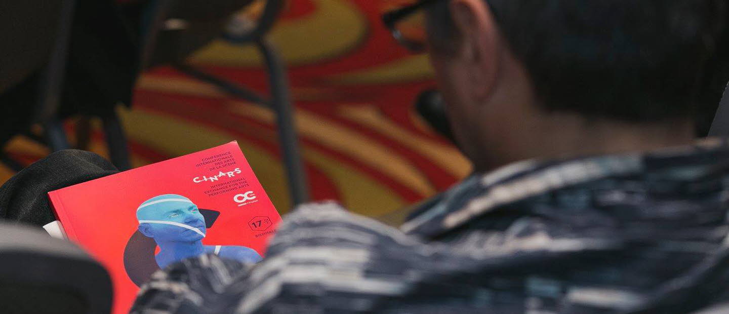 Foto av en man bakifrån som sitter och tittar på programmet för Cinars. Omslaget är rött med en blå man från axlarna och uppåt.