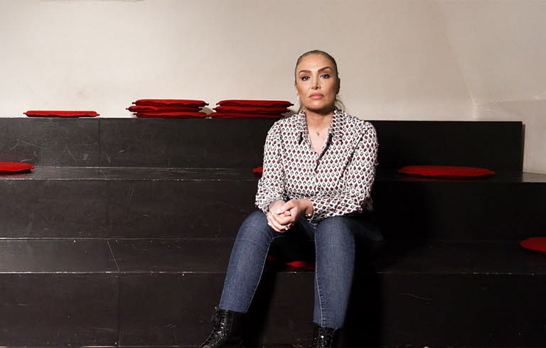 Kvinna sitter ner på en gradäng och tittar in i kameran.