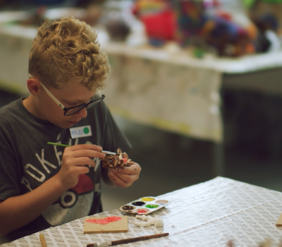 Pojke sitter vid ett bord och målar på figurer.