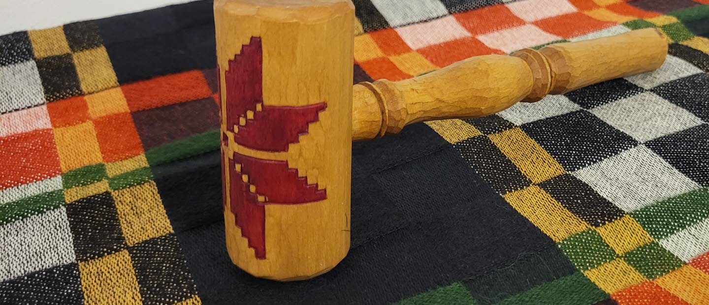 Träklubba dekorerad med röd stjärna, liggande på en färgglad rutmönstrad textil.