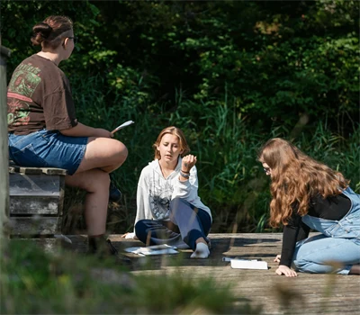 Ungdomar med böcker som sitter och pratar på ett trädäck.