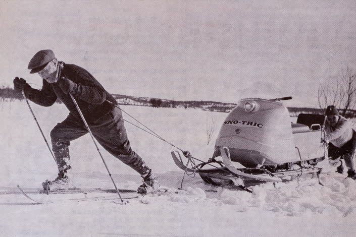 Man på arkivfoto på skidor som drar en skoter. 