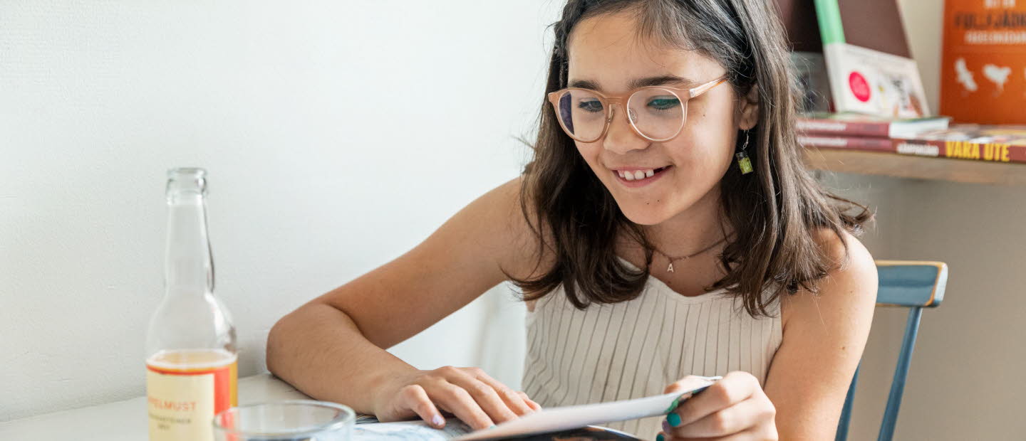 Flicka läser bok vid köksbordet