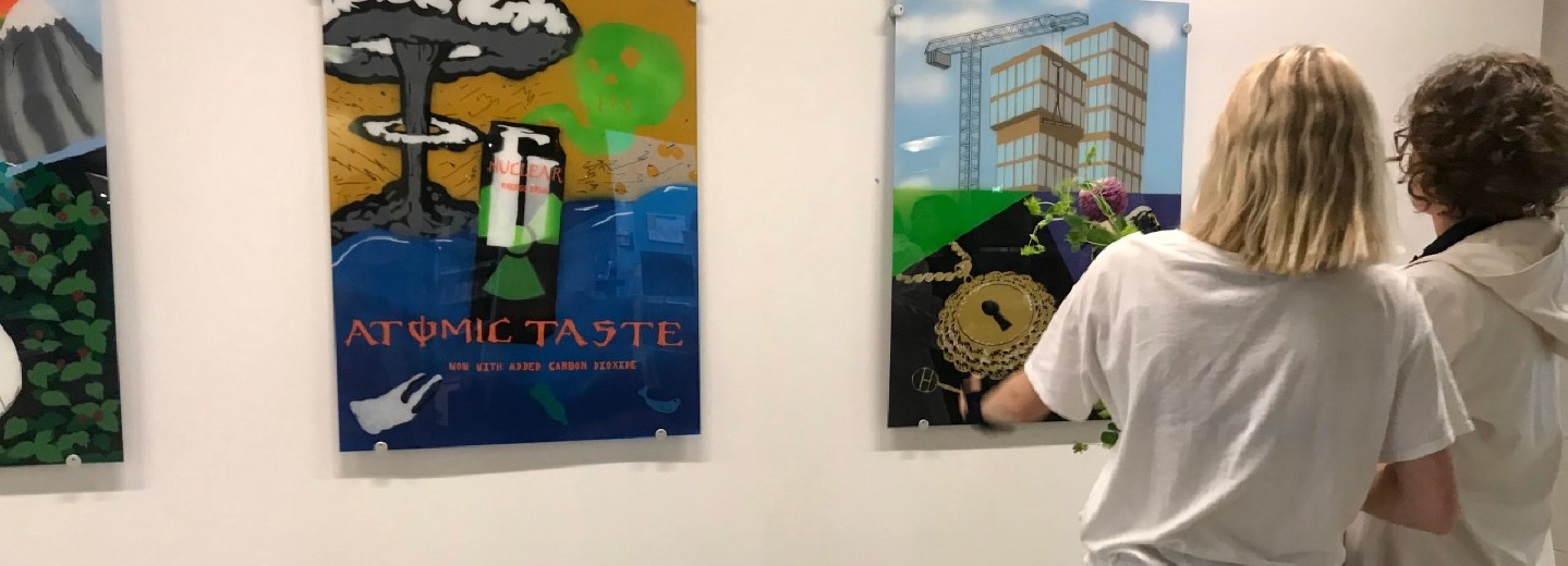 Två personer ser på tavlor som hänger på en vägg.