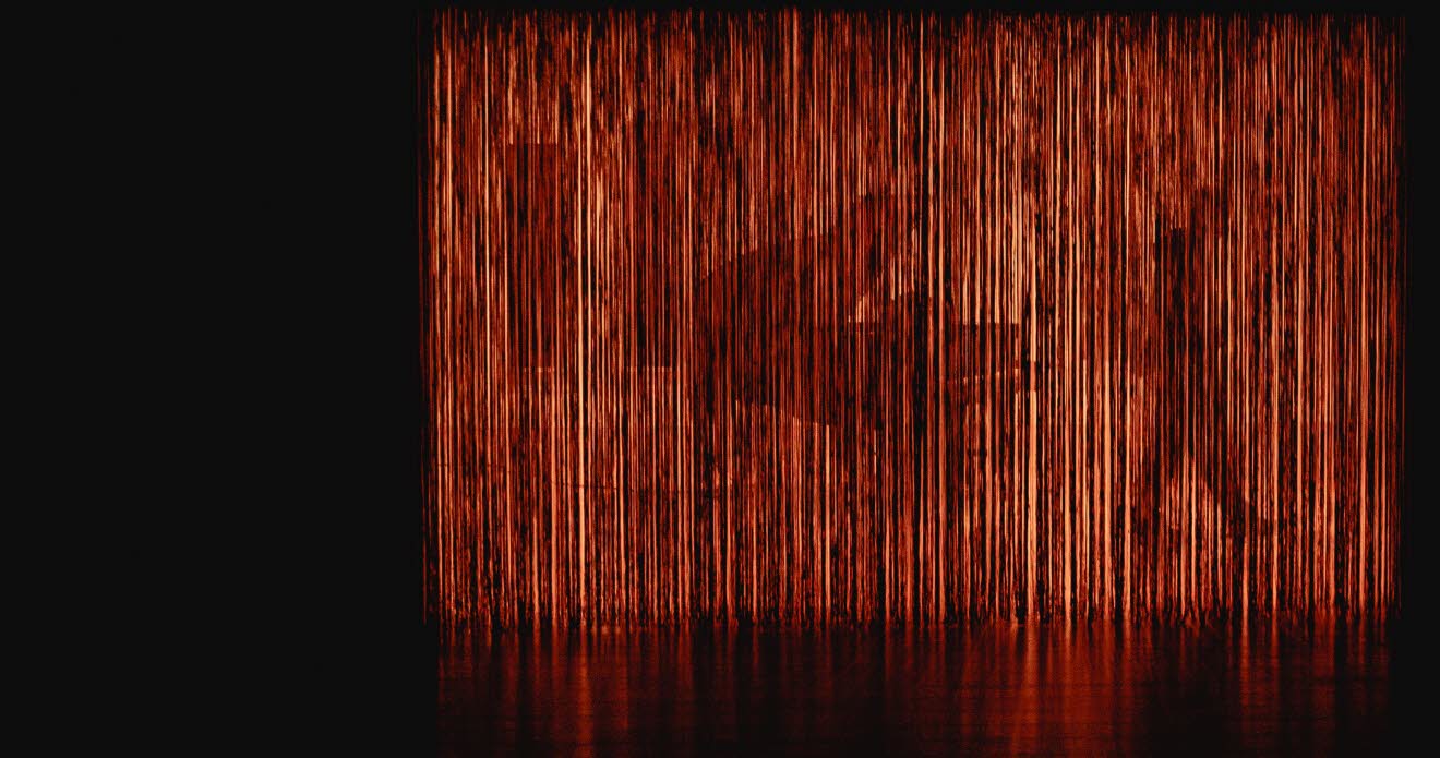 Silhuetten av en flygel och en gående person skymtar bakom ett upplyst tyg.