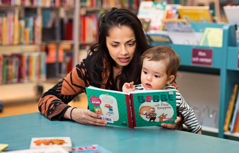 Kvinna och barn sitter vid ett litet bord på ett bibliotek och titta i en pekbok.