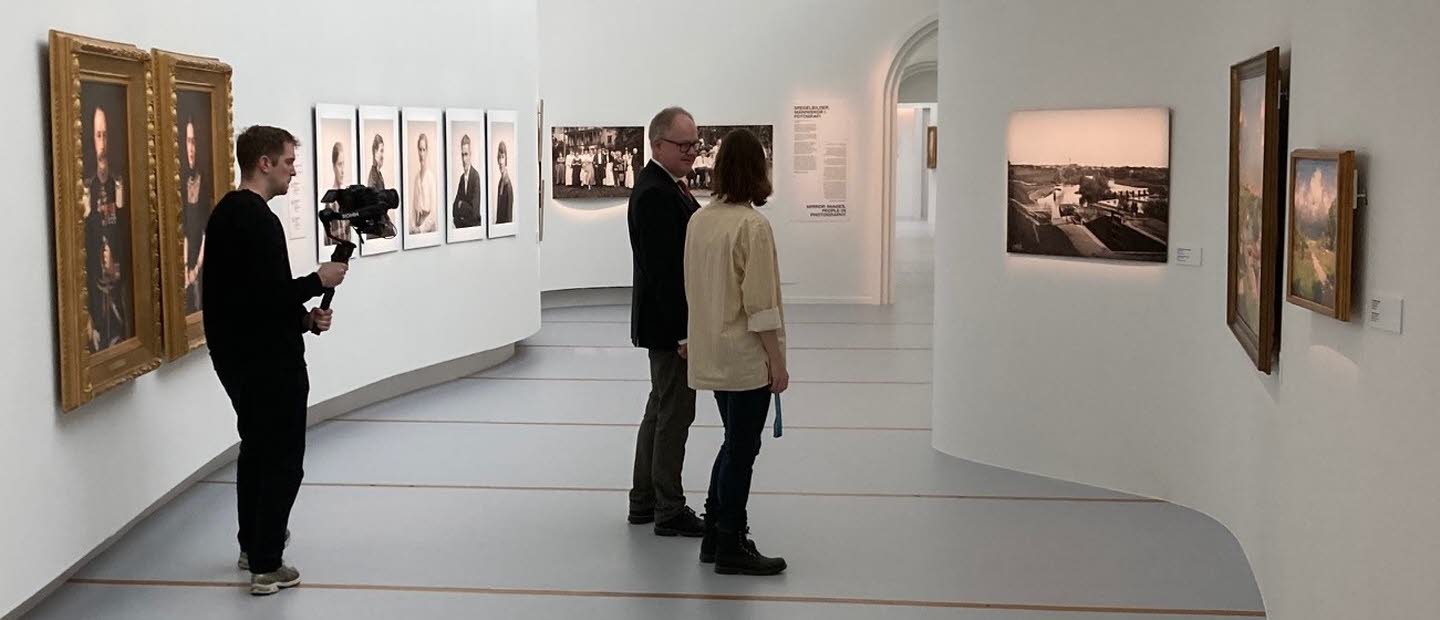 Två personer tittar på konst på Östergötlands museum. I bakgrunden står en filmare och filmar.