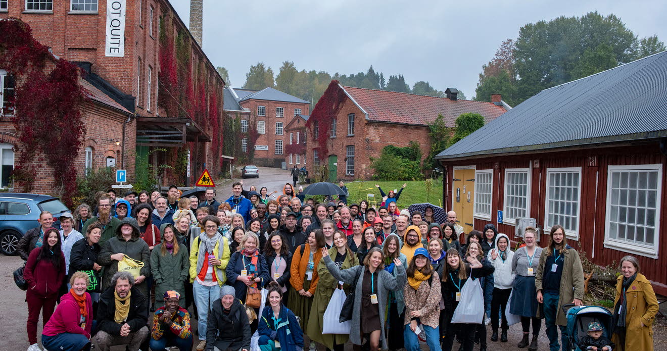 Gruppbild utomhus. I bakgrunden syns ett rött trähus och flera tegelhus.