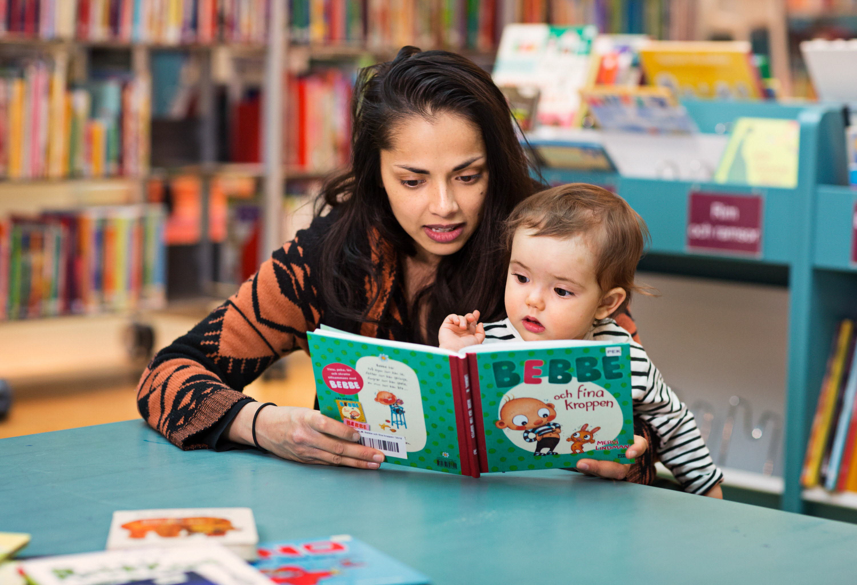 Kvinna och barn sitter vid ett litet bord på ett bibliotek och titta i en pekbok.