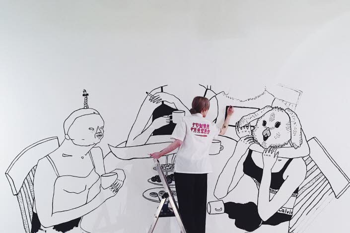Bim Eriksson is painting on a wall. She's painting four women sitting att a dinner table.
